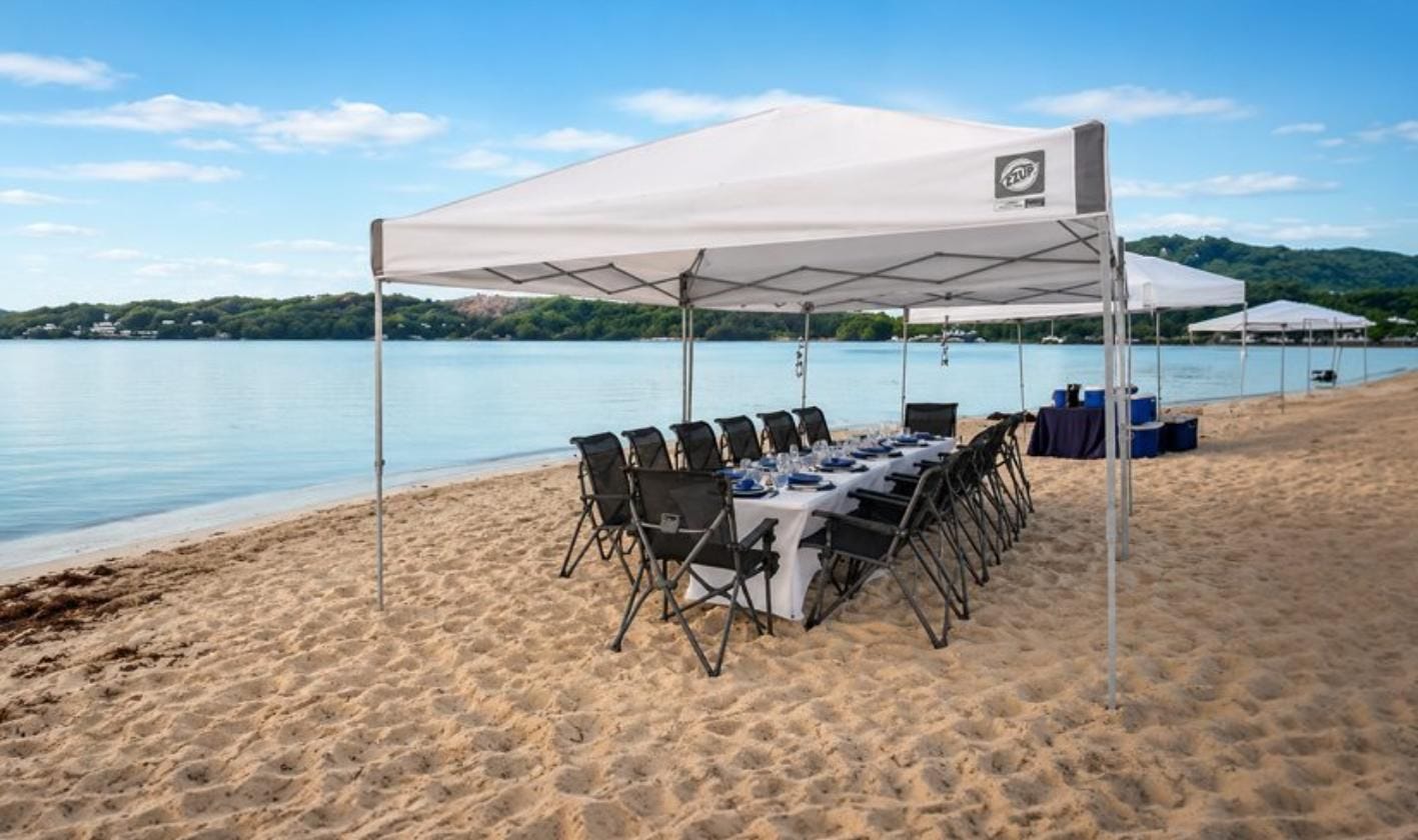 Large canopy tent with seating arrangement on a beach, illustrating guest capacity and space planning for 10x10, 10x15, and 10x20 canopy tents.
